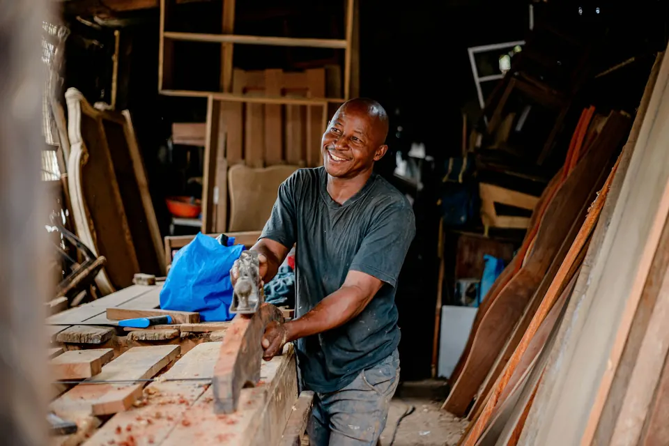 Menuisier souriant rabotant une planche dans son atelier encombré de bois