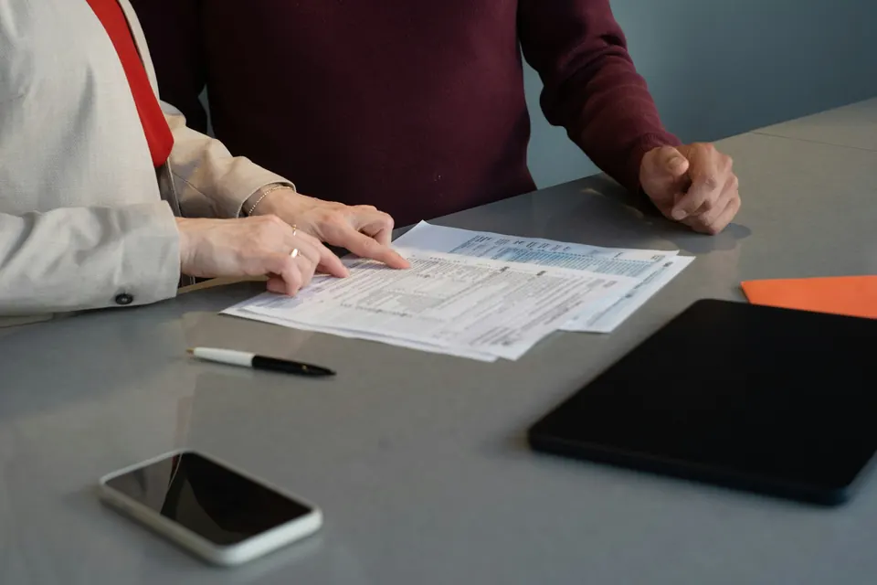 Deux personnes relisent des documents posés sur une table, un stylo et un téléphone à côté
